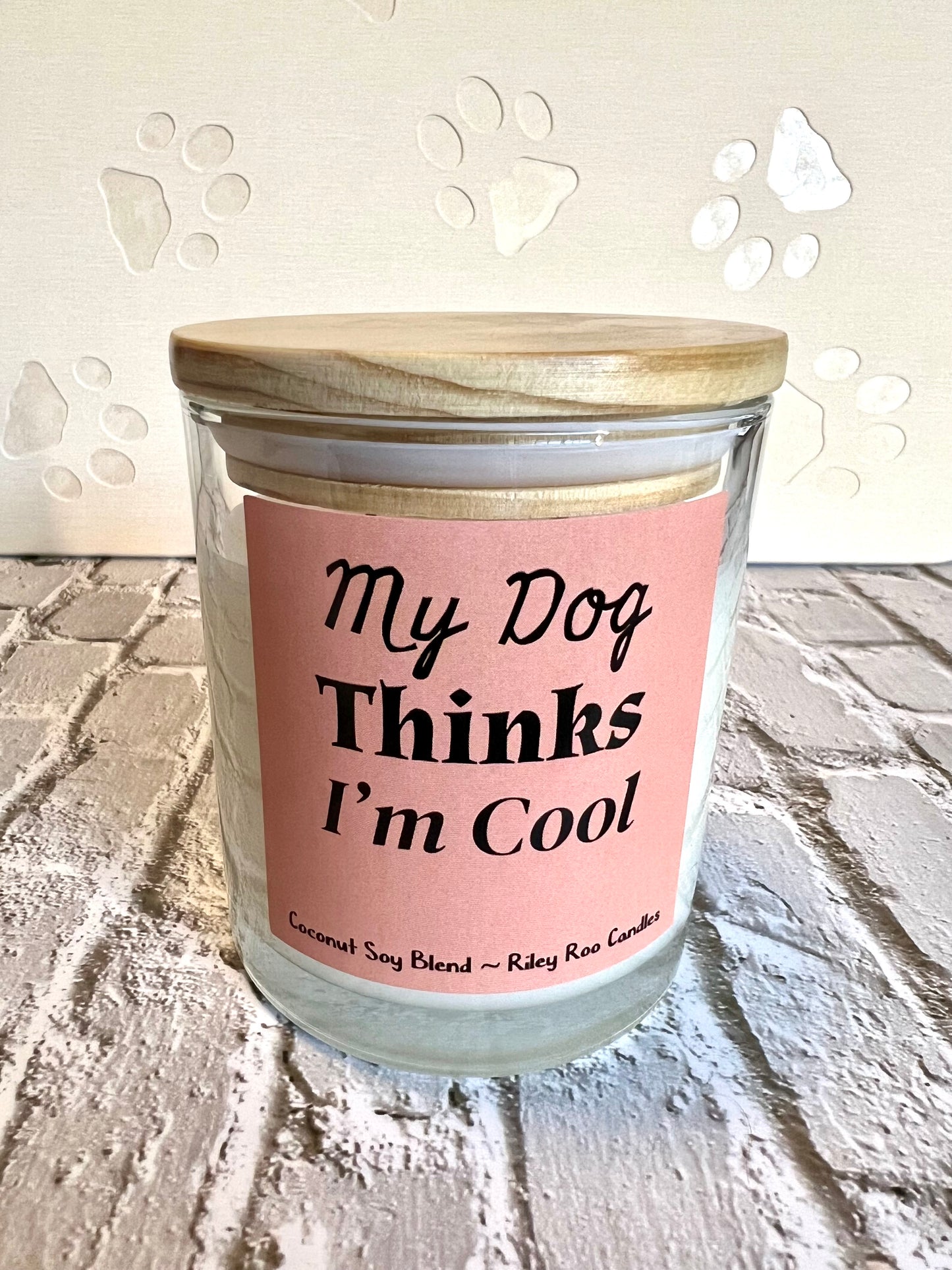 Candle with a pink label reading 'My Dog Thinks I'm Cool' on a textured surface.
