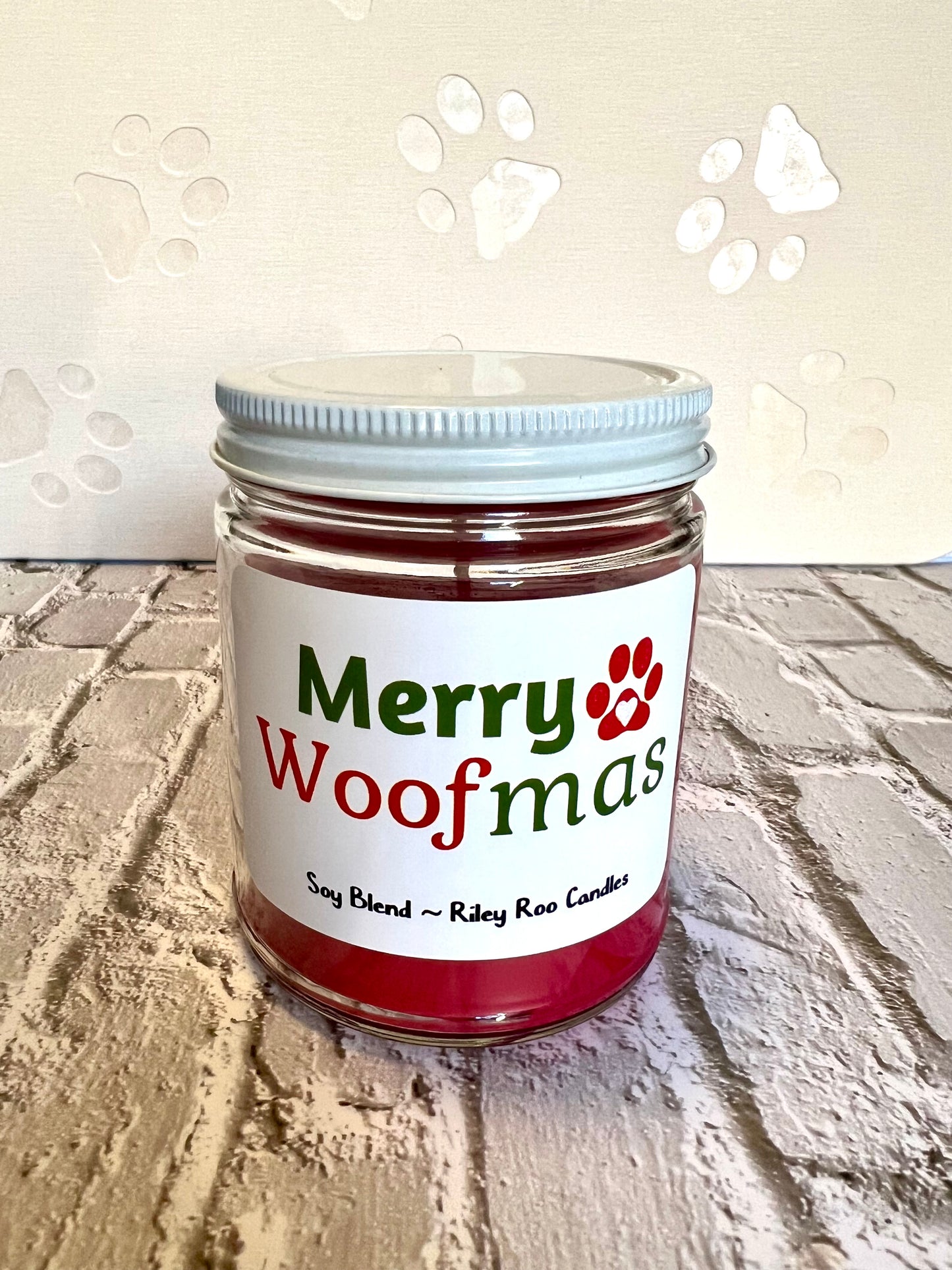 Jar of candle labeled 'Merry Woofmas' on a textured surface with paw print designs.