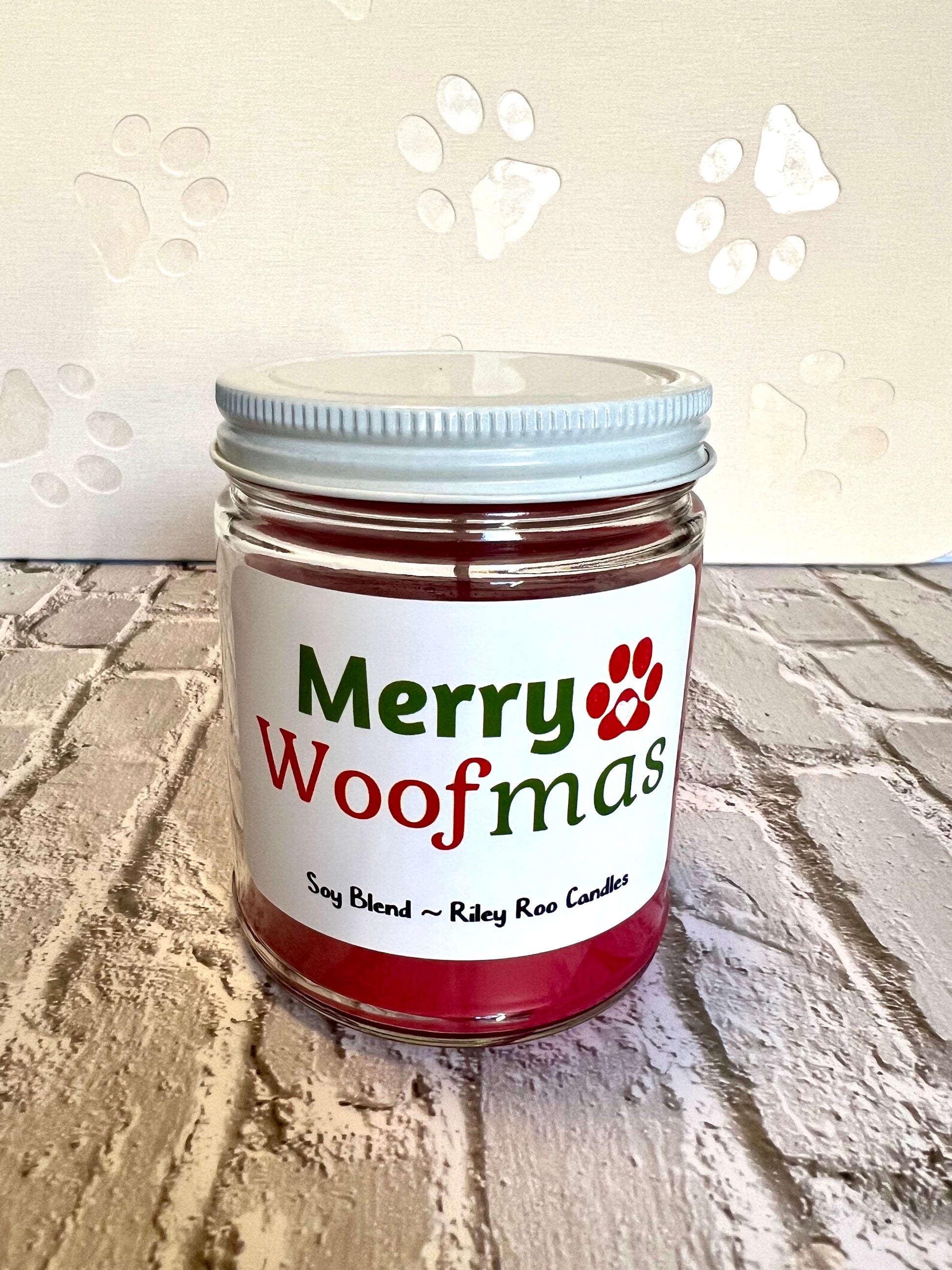 Jar of candle labeled 'Merry Woofmas' on a textured surface with paw print designs.