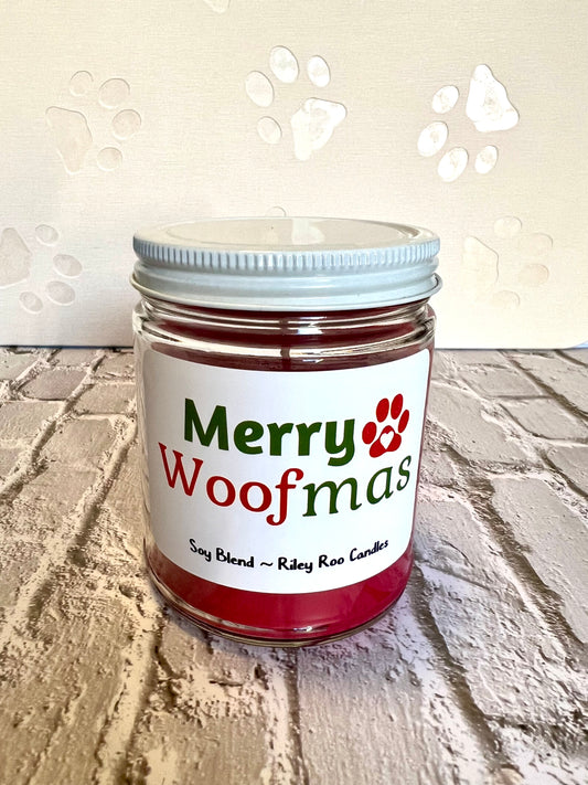 Jar of candle labeled 'Merry Woofmas' on a textured surface with paw print designs.