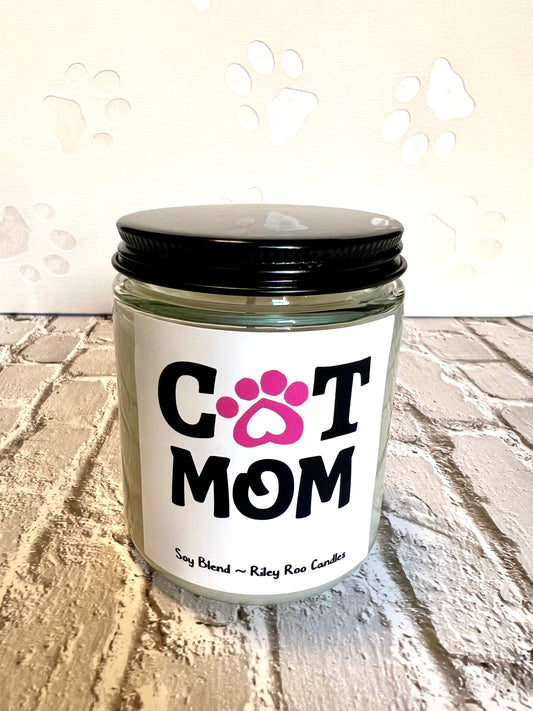Candle jar labeled 'Cat Mom' on a textured surface with paw prints in the background